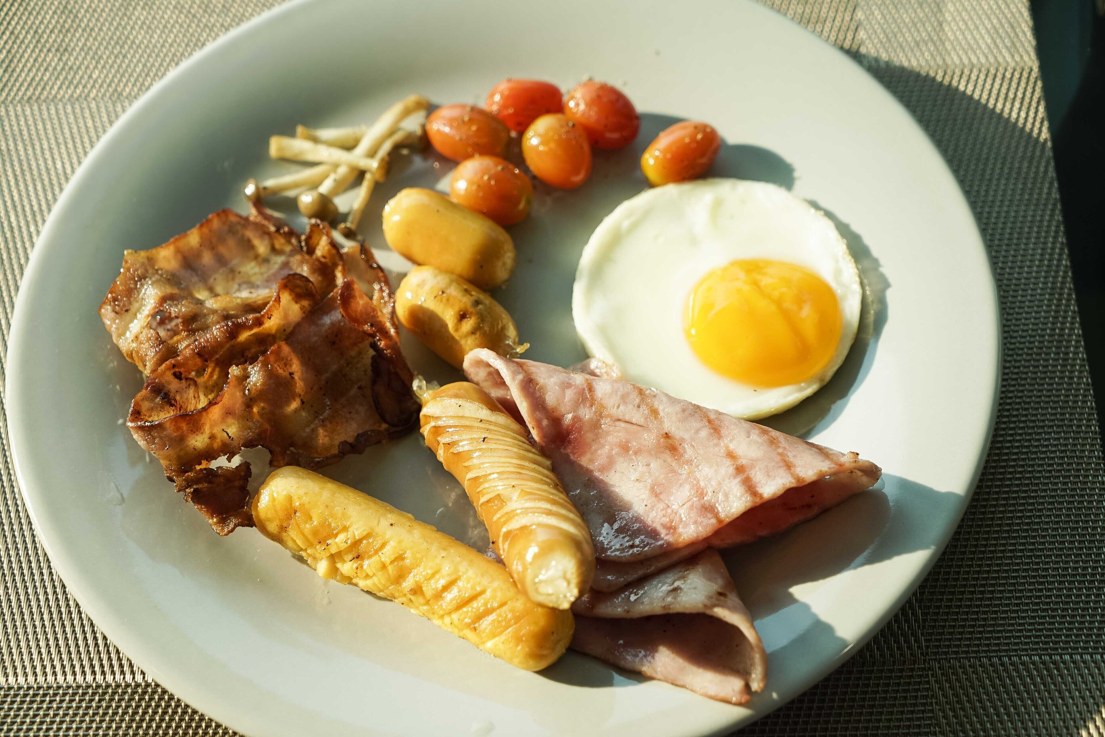 A plate with bacon, ham, eggs, sausages, and tomatoes.