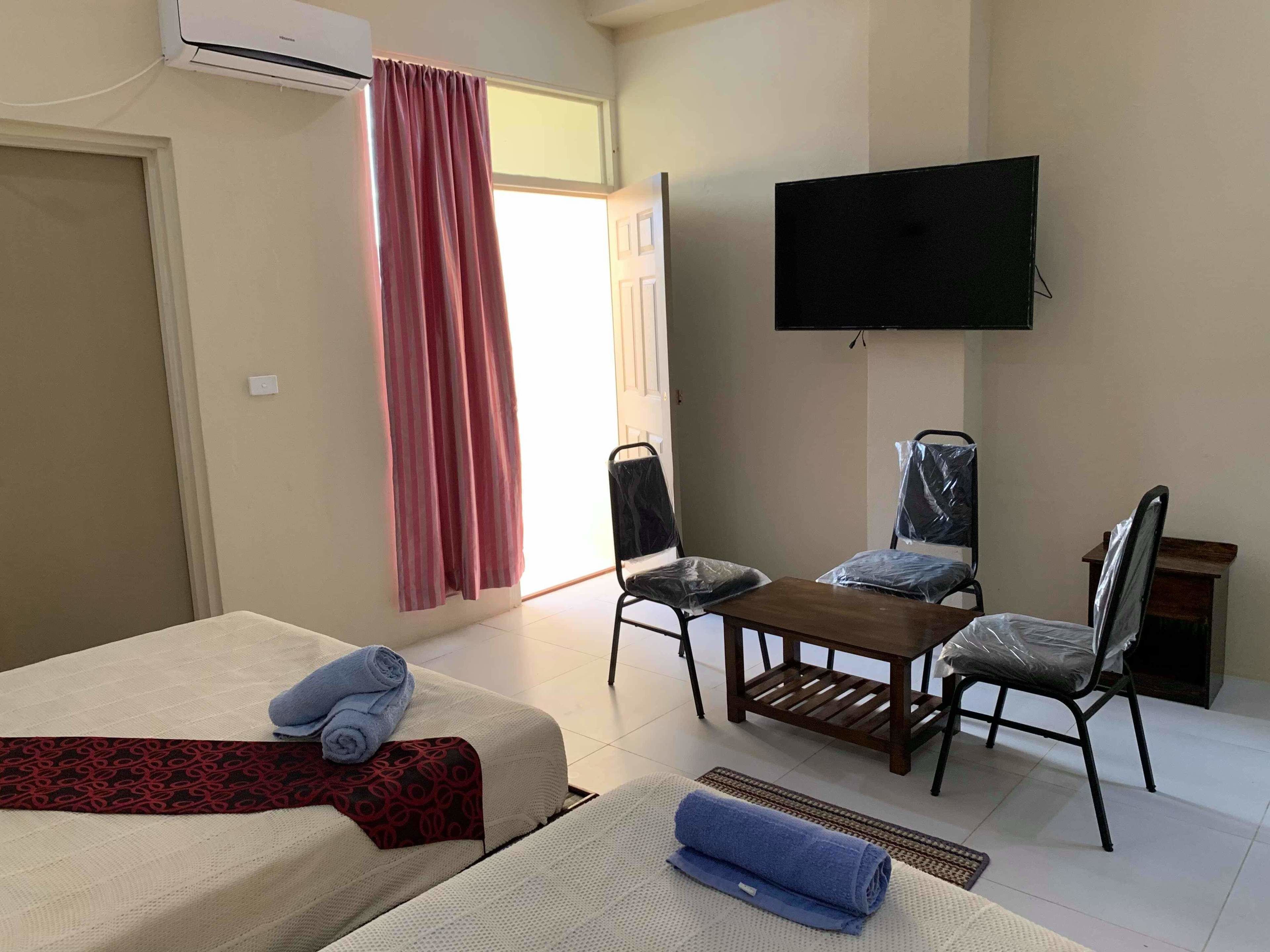 Habitación de hotel con cama, escritorio, dos sillas, televisor y ventana con cortinas.