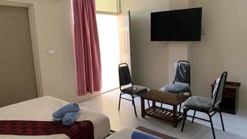 Une chambre d’hôtel avec un lit, un bureau, deux chaises, une télévision et une fenêtre avec des rideaux.