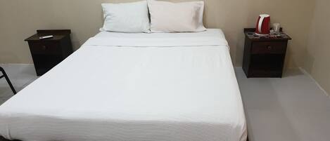 Ein ordentlich bezogenes Bett mit weißer Bettwäsche, zwei Nachttische und ein rotes und weißes Objekt auf dem rechten Tisch.