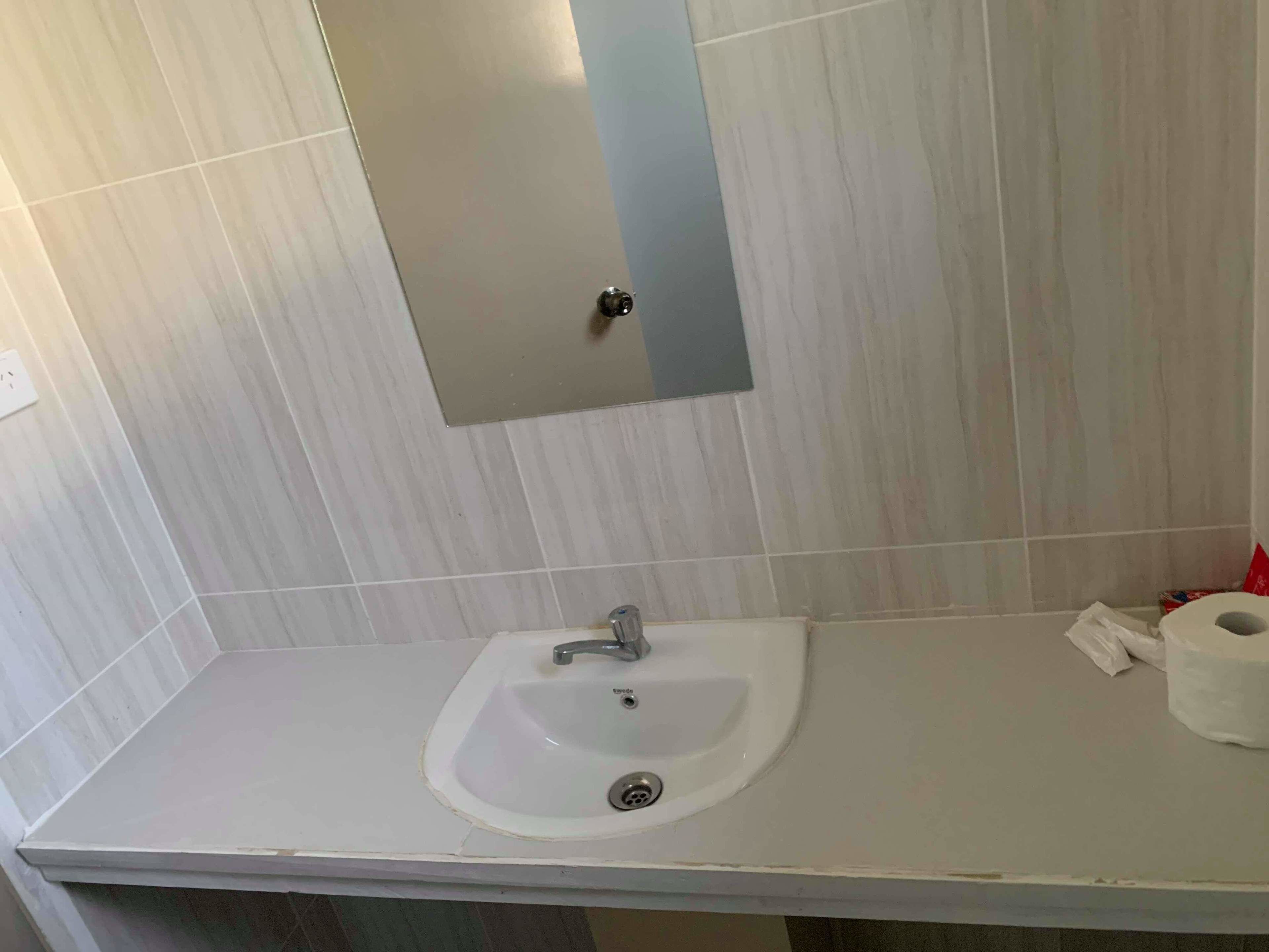 Une salle de bain avec un lavabo blanc, un miroir et un rouleau de papier toilette.
