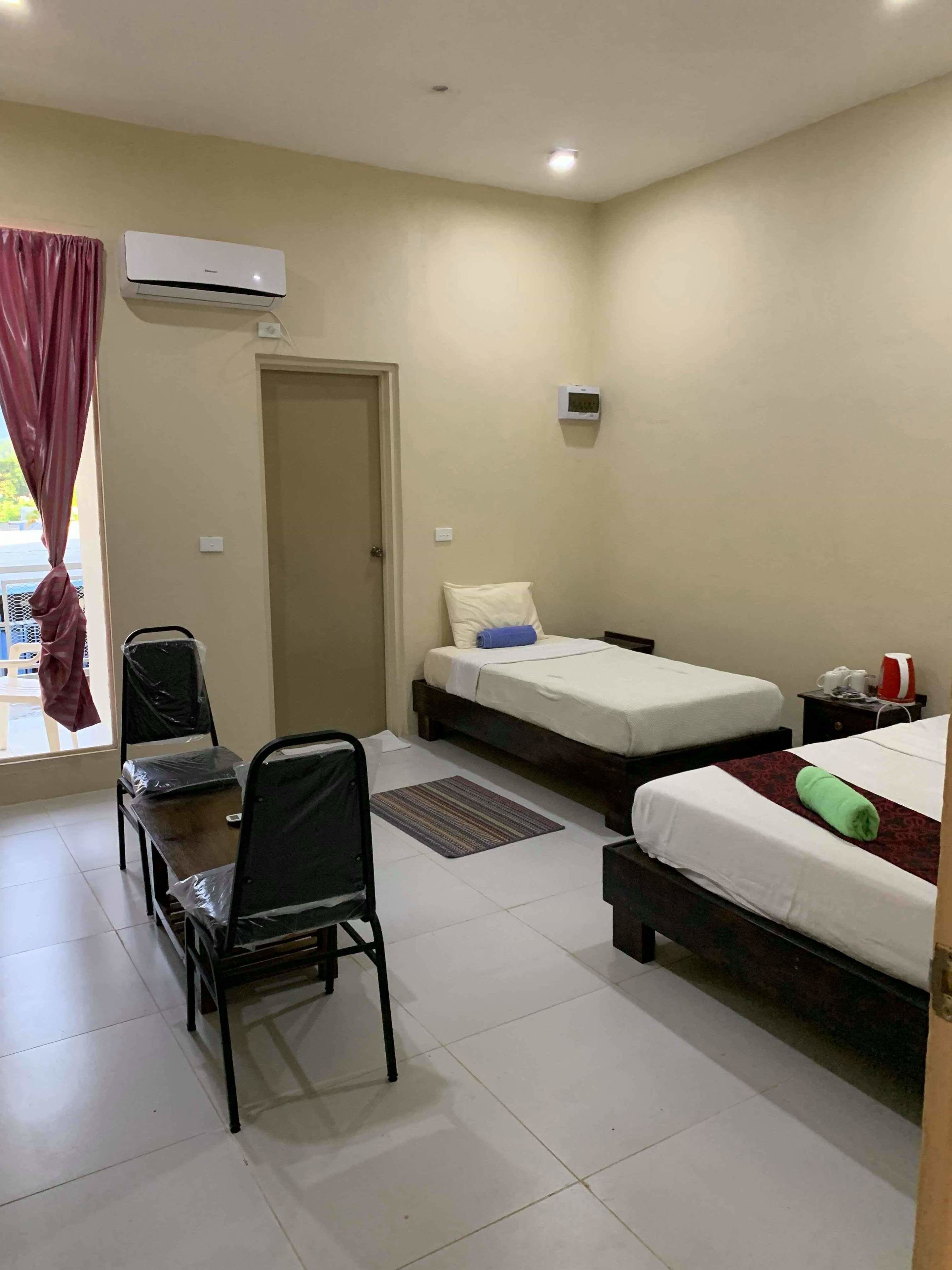 Habitación de hotel con dos camas, un escritorio, una silla, aire acondicionado y una ventana con cortinas.