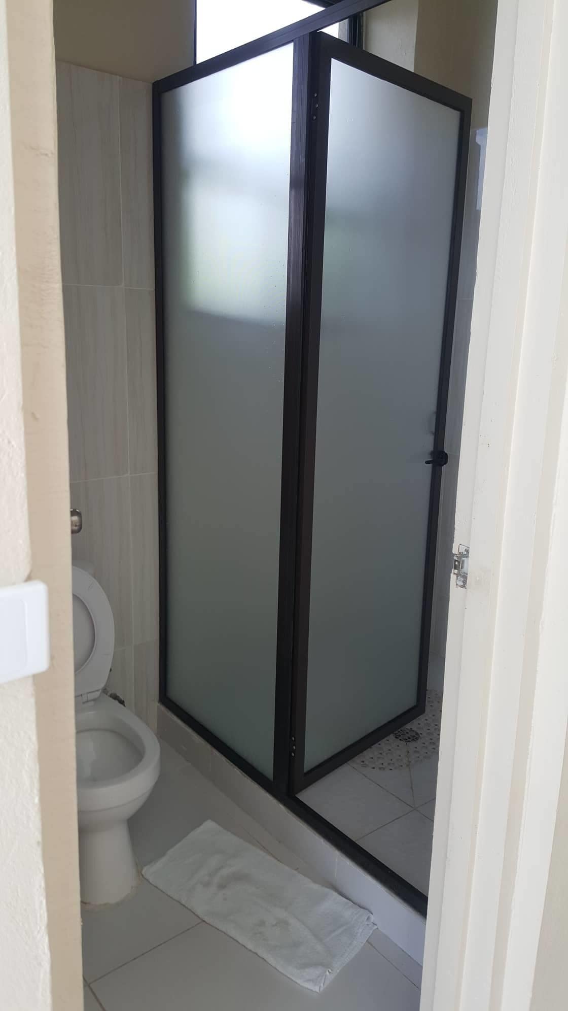 A bathroom with a glass-enclosed shower, a toilet, and a white towel on the floor.