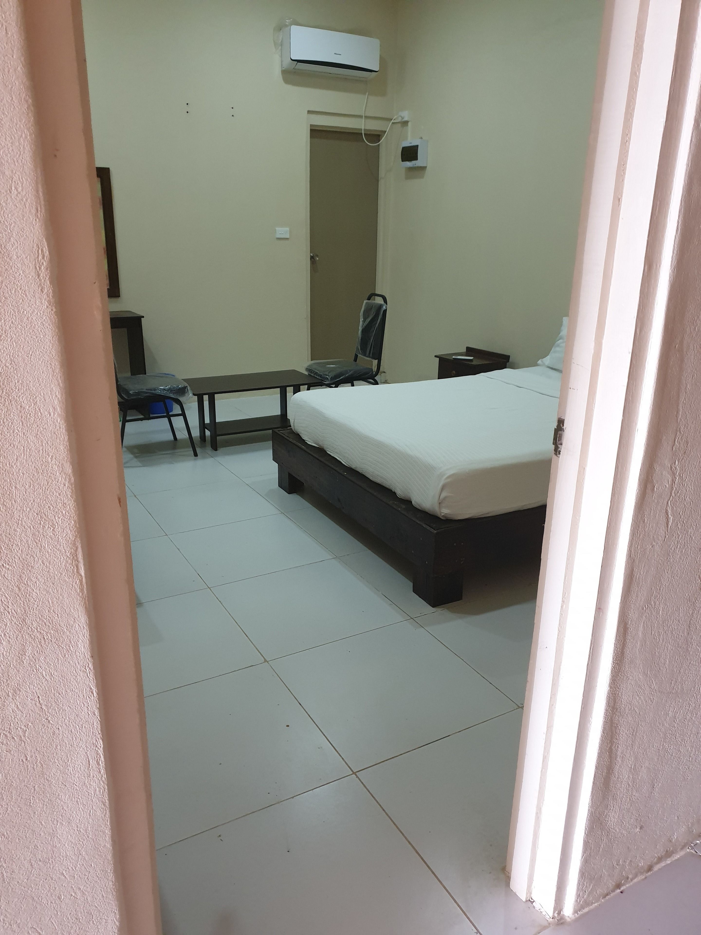 A bedroom with a bed, a chair, a desk, and an air conditioning unit.