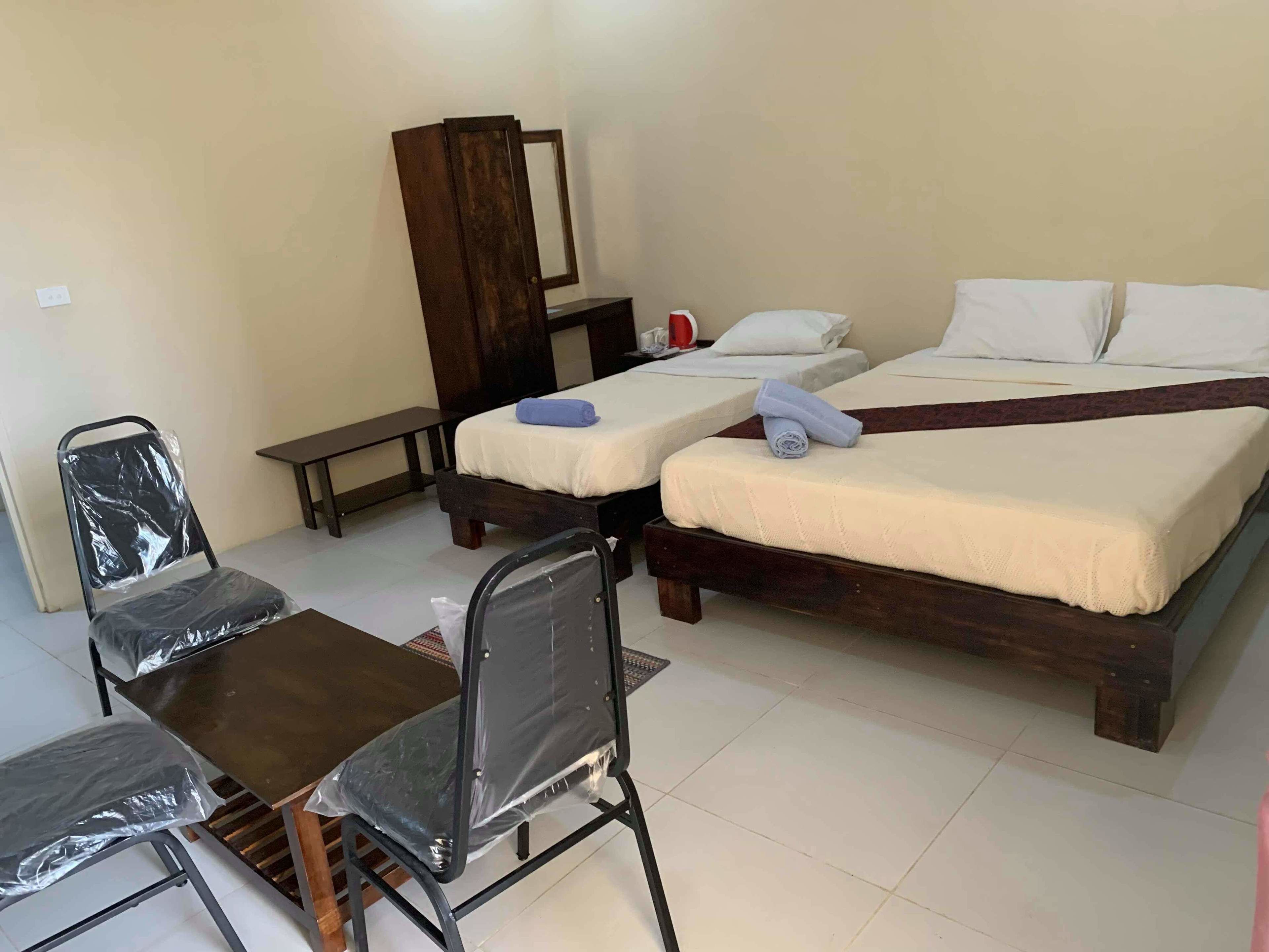 A room with two single beds, a wooden desk, a chair, a mirror, and a small table.