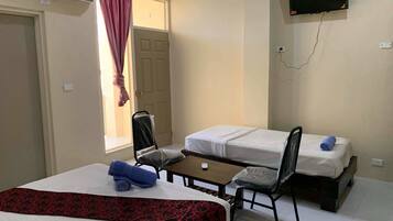 Ein Hotelzimmer mit zwei Betten, einem Schreibtisch, einem Sessel, einem an der Wand montierten Fernseher und einer Klimaanlage.