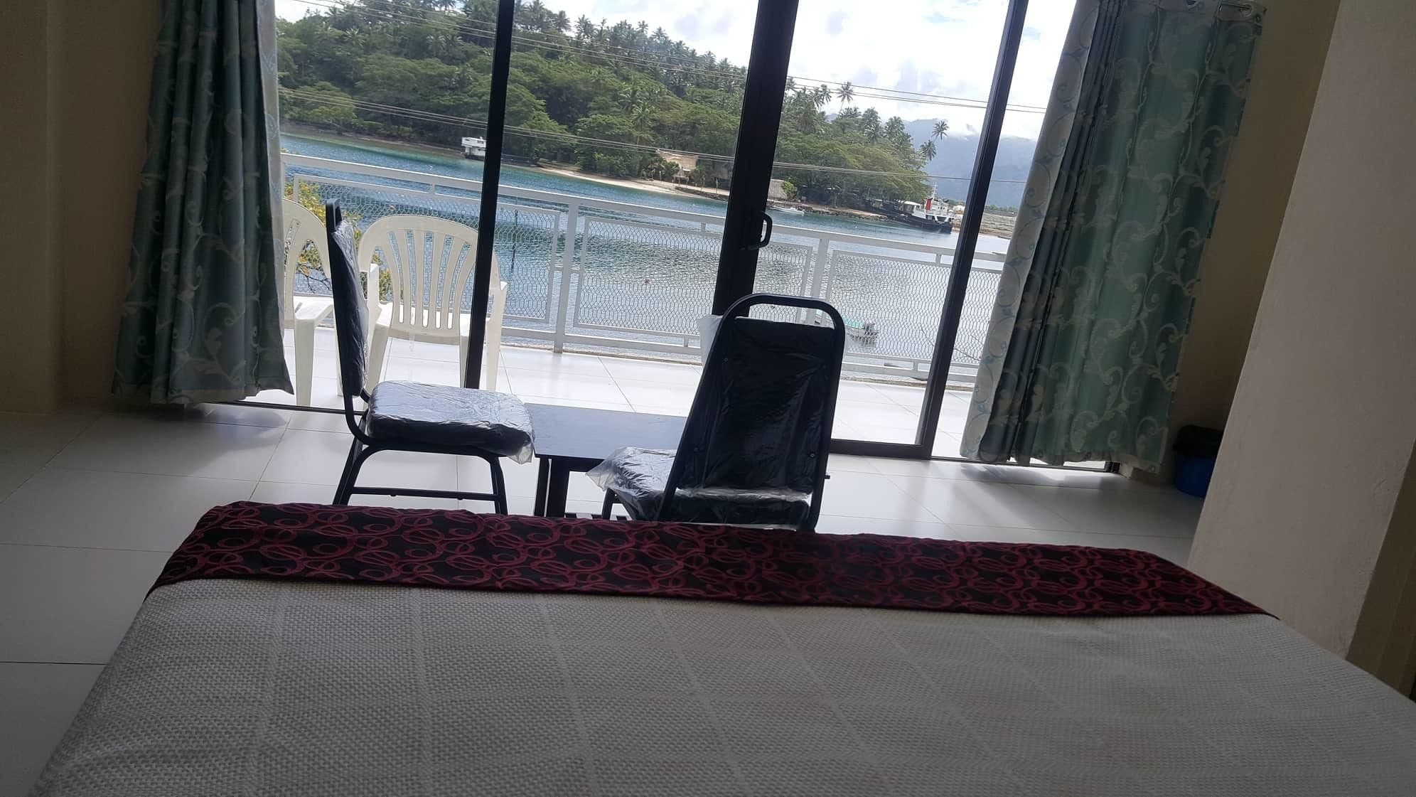 Une chambre d’hôtel avec un lit, une table et deux chaises. La chambre dispose d’une grande fenêtre donnant sur un plan d’eau et sur la verdure.