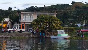 A building with a balcony, a tree in front, and a body of water with boats. - Bay View Barbers Lodge (Savusavu)