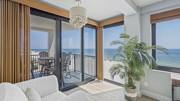 Uma varanda com vista para a praia, um sofá branco e um vaso de planta.