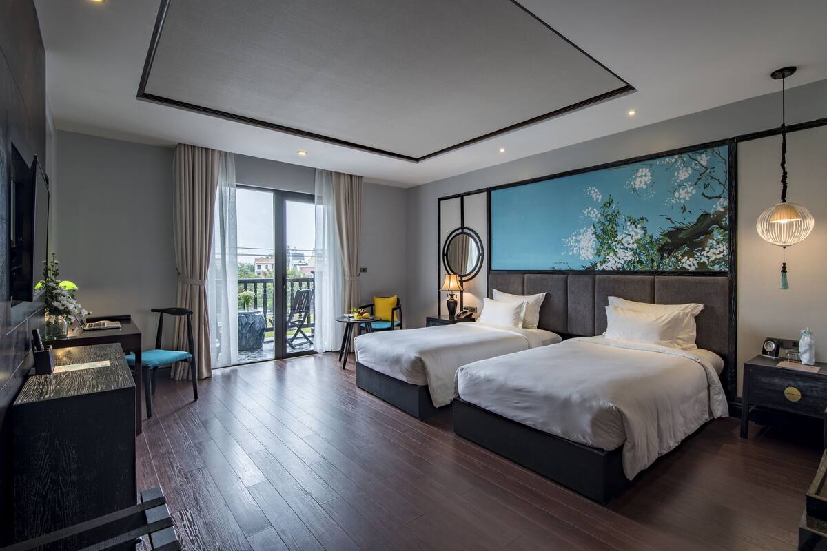 Ein modernes Hotelzimmer mit zwei Betten, einem Schreibtisch, einem Fernseher und einem großen Fenster mit Vorhängen.