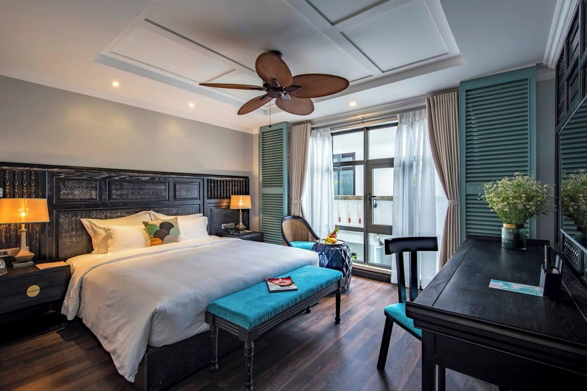 Ein Hotelzimmer mit Bett, Schreibtisch, Stuhl, Deckenventilator und einem Fenster mit Vorhängen.