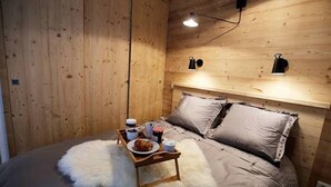 Ett mysigt sovrum med en sänggavel i trä, en mjuk, vit matta och ett nattduksbord med en tallrik mat och dryck.