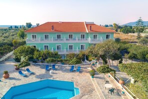A large building with a red-tiled roof and a pool area with blue lounge chairs.