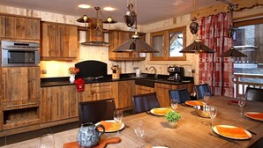 Interior de madera con una mesa de comedor para cuatro personas, electrodomésticos de cocina e iluminación colgante.