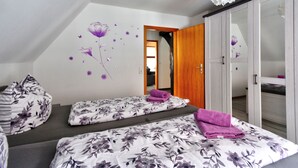 A bedroom with two beds, floral bedding, a wooden wardrobe, and a ceiling light fixture.