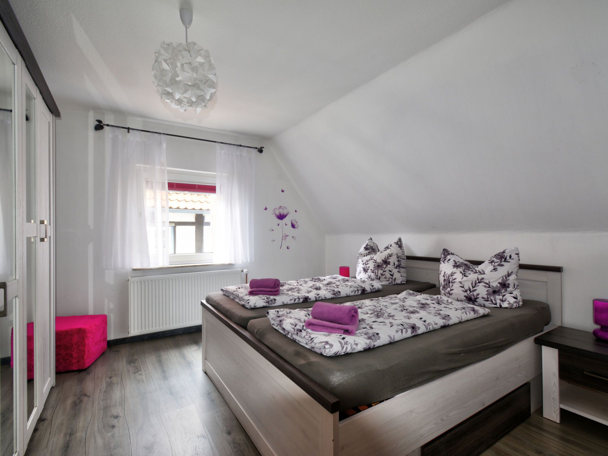 Una camera da letto con un letto, una finestra con tende, un termosifone e una lampada a soffitto.