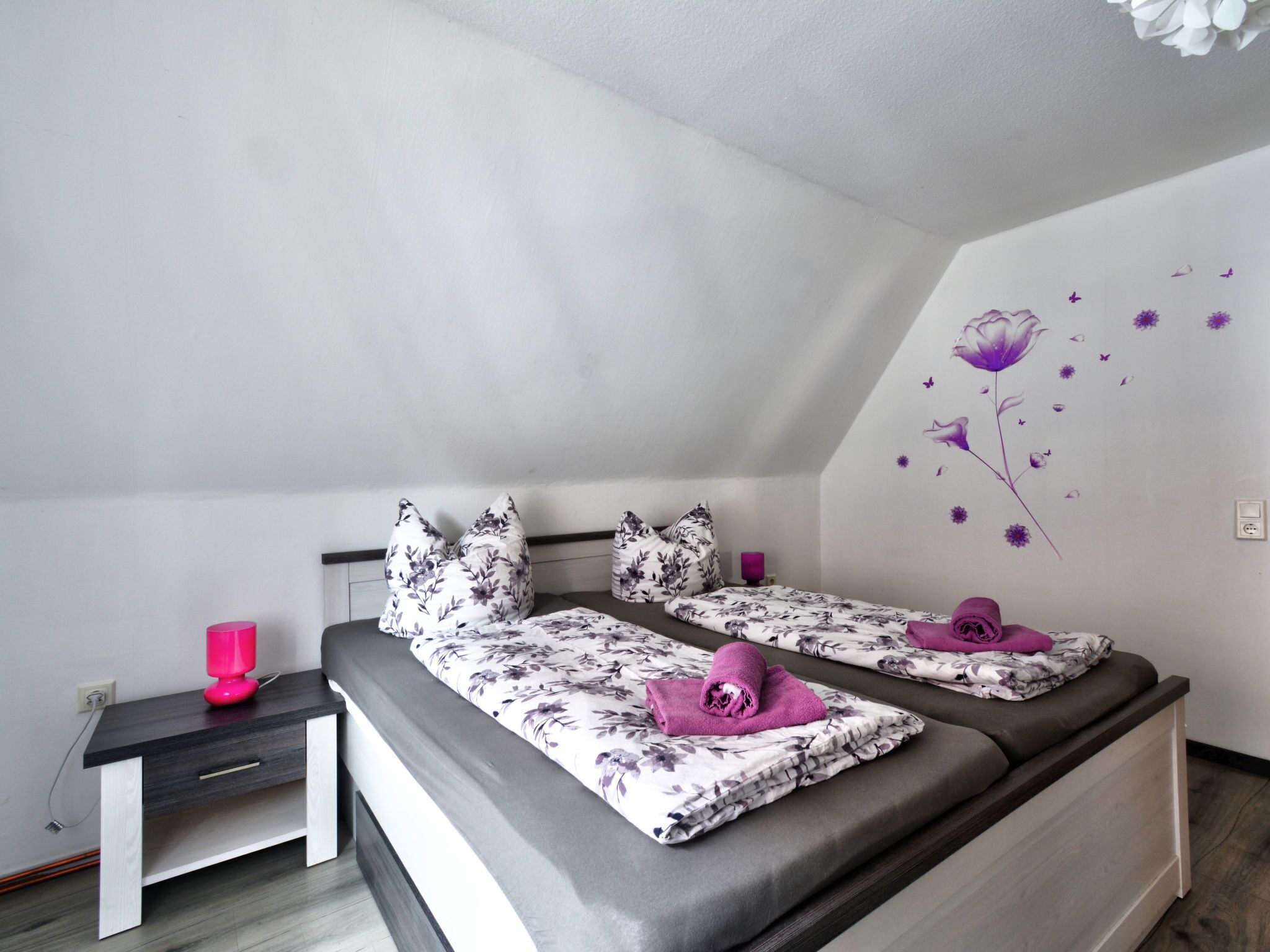 A bedroom with two beds, a nightstand, and a wall with floral decals.