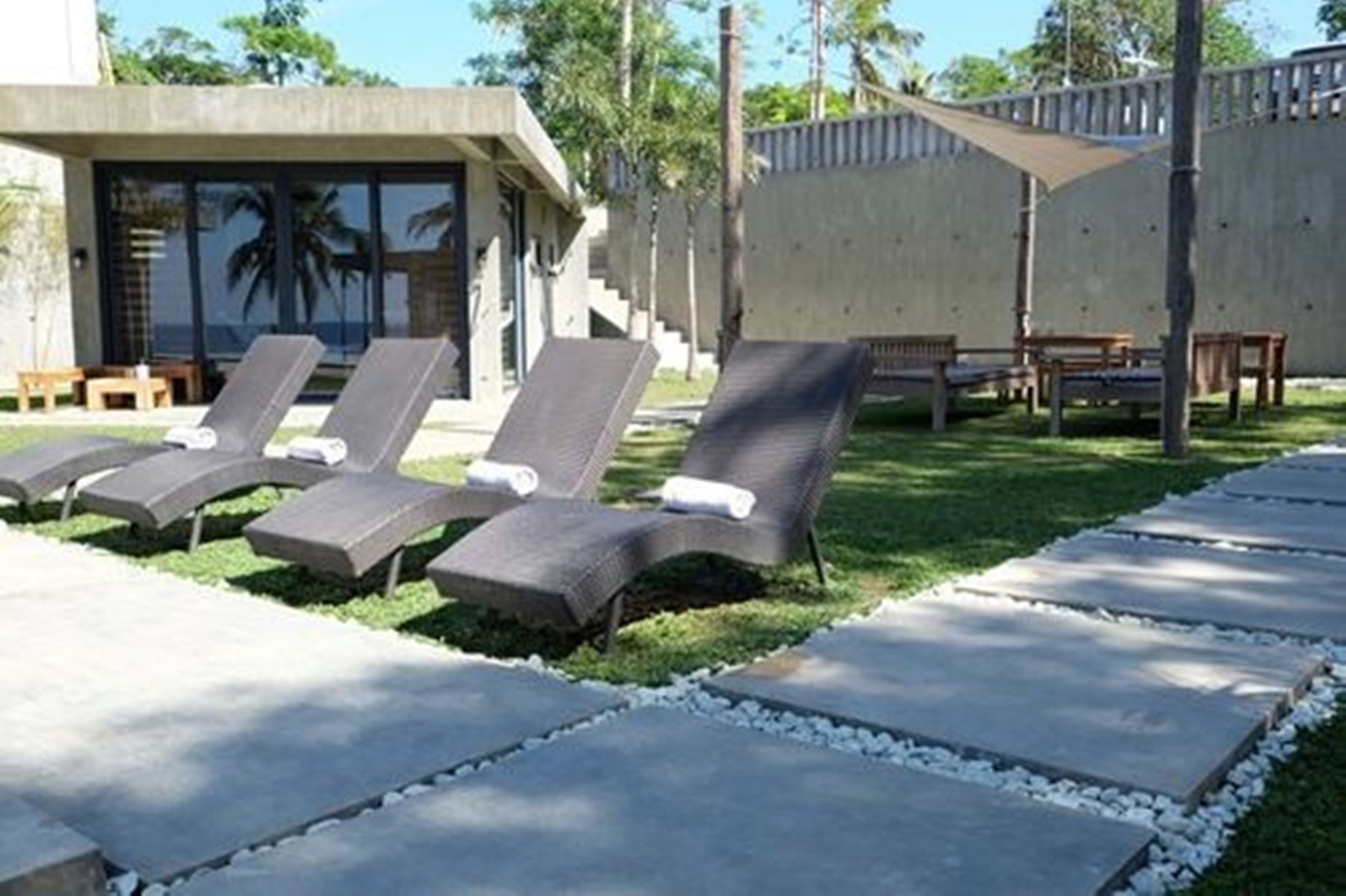 Zona de piscina con sillones de descanso y un camino de hormigón.