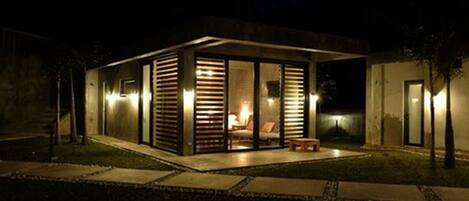Una casa moderna con cerramiento de vidrio, un dormitorio a la vista con una cama y un pequeño espacio de estar al aire libre.