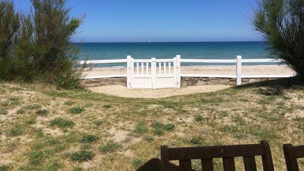 A beach view with a white gate leading to the shore, surrounded by sparse vegetation. - House ALL COMFORT, NICE GARDEN, FEET IN THE WATER, DIRECT BEACH ACCESS (La Hague)