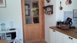 A kitchen with a wooden door, white cabinets, and copper cookware hanging on the wall. - House ALL COMFORT, NICE GARDEN, FEET IN THE WATER, DIRECT BEACH ACCESS (La Hague)