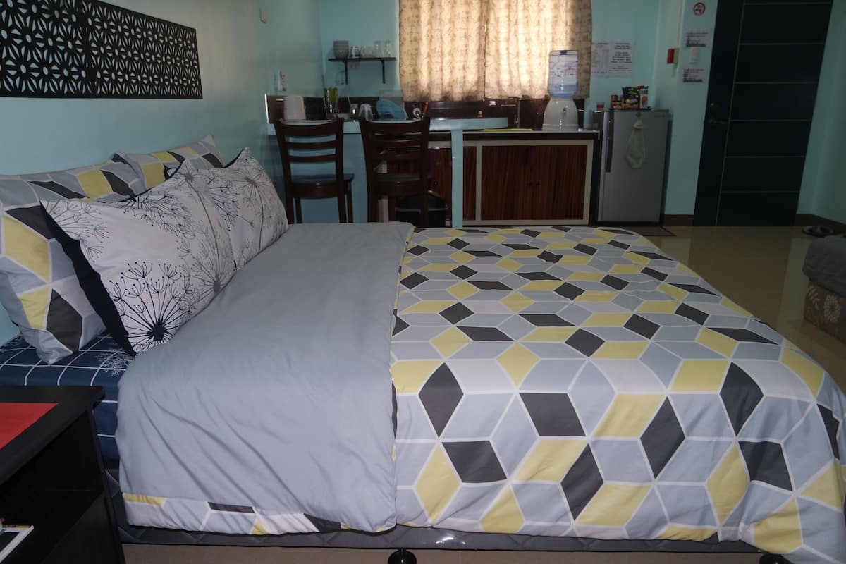 Quarto de hotel com cama, escrivaninha e cozinha compacta.
