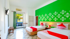 A hotel room with two beds, a green accent wall, and a view of the outdoors. - OYO 1206 Lombok Guest House (Mataram)