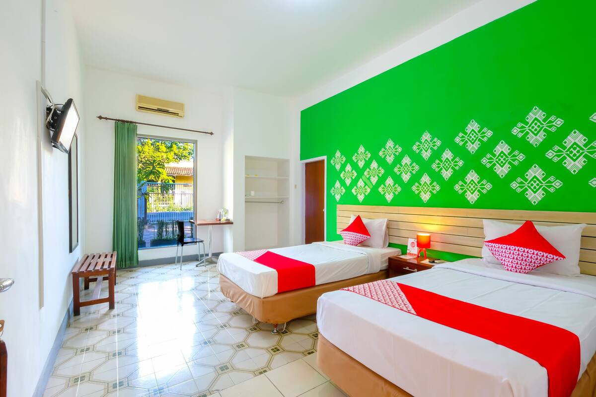 A hotel room with two beds, a green accent wall, and a view of the outdoors.