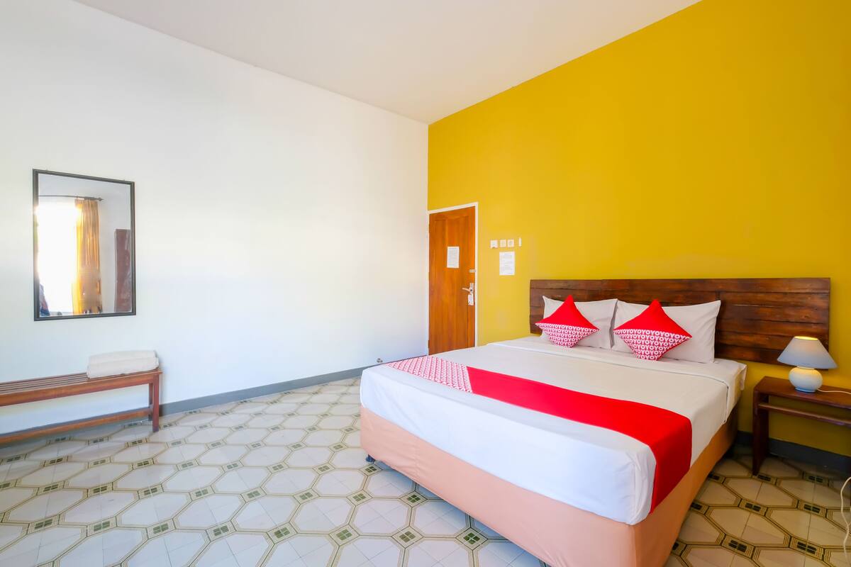 A hotel room with a bed, a bench, a nightstand, and a mirror.