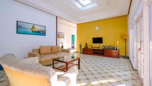 A living room with a sofa, coffee table, and a TV. There is a yellow wall and a clock. - OYO 1206 Lombok Guest House (Mataram)