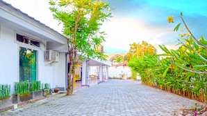 A cobblestone pathway leading to a building with a covered entrance and a small garden area with potted plants and a tree. - OYO 1206 Lombok Guest House (Mataram)