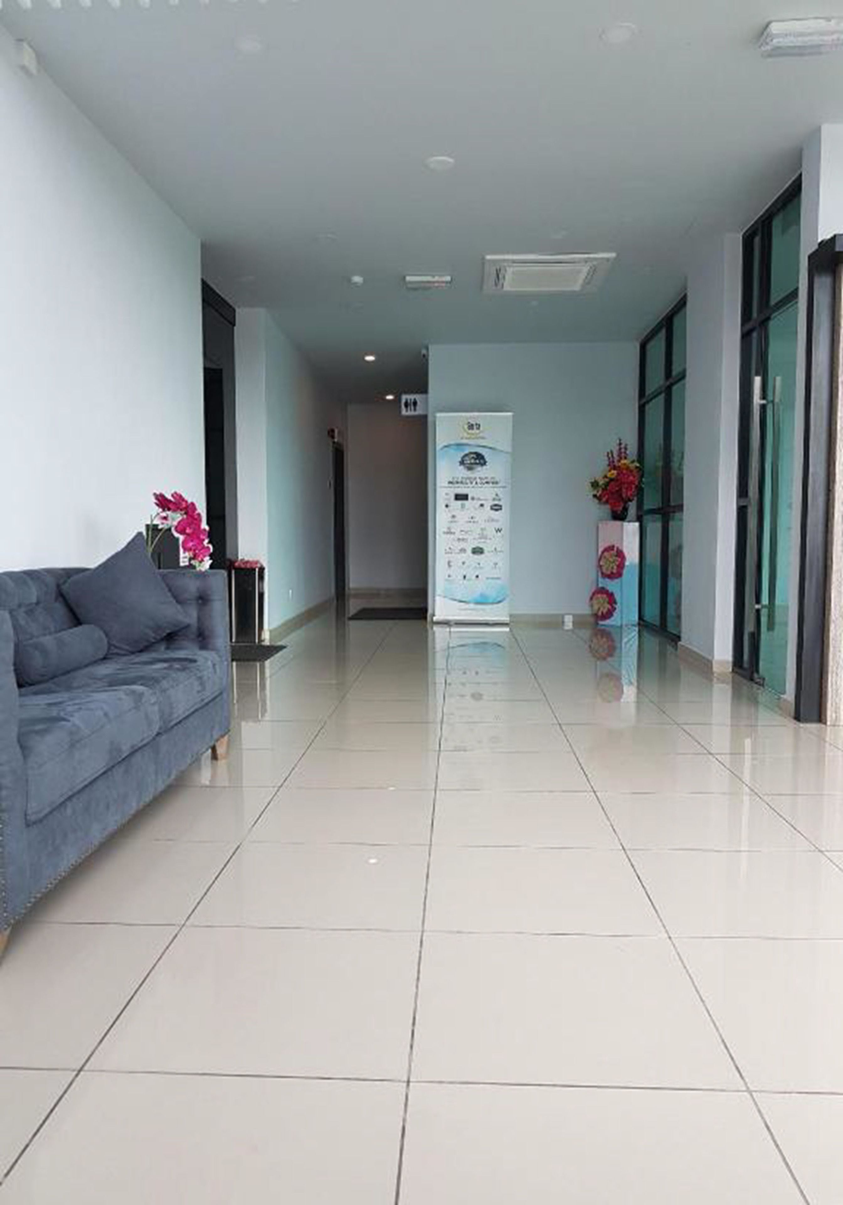 A clean, modern hotel lobby with a grey sofa, a reception desk, and a glass door entrance.