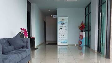 A clean, modern hotel lobby with a grey sofa, a reception desk, and a glass door entrance.