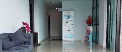 Un vestíbulo de hotel moderno y limpio, con un sofá gris, una recepción y un acceso por puerta de cristal.
