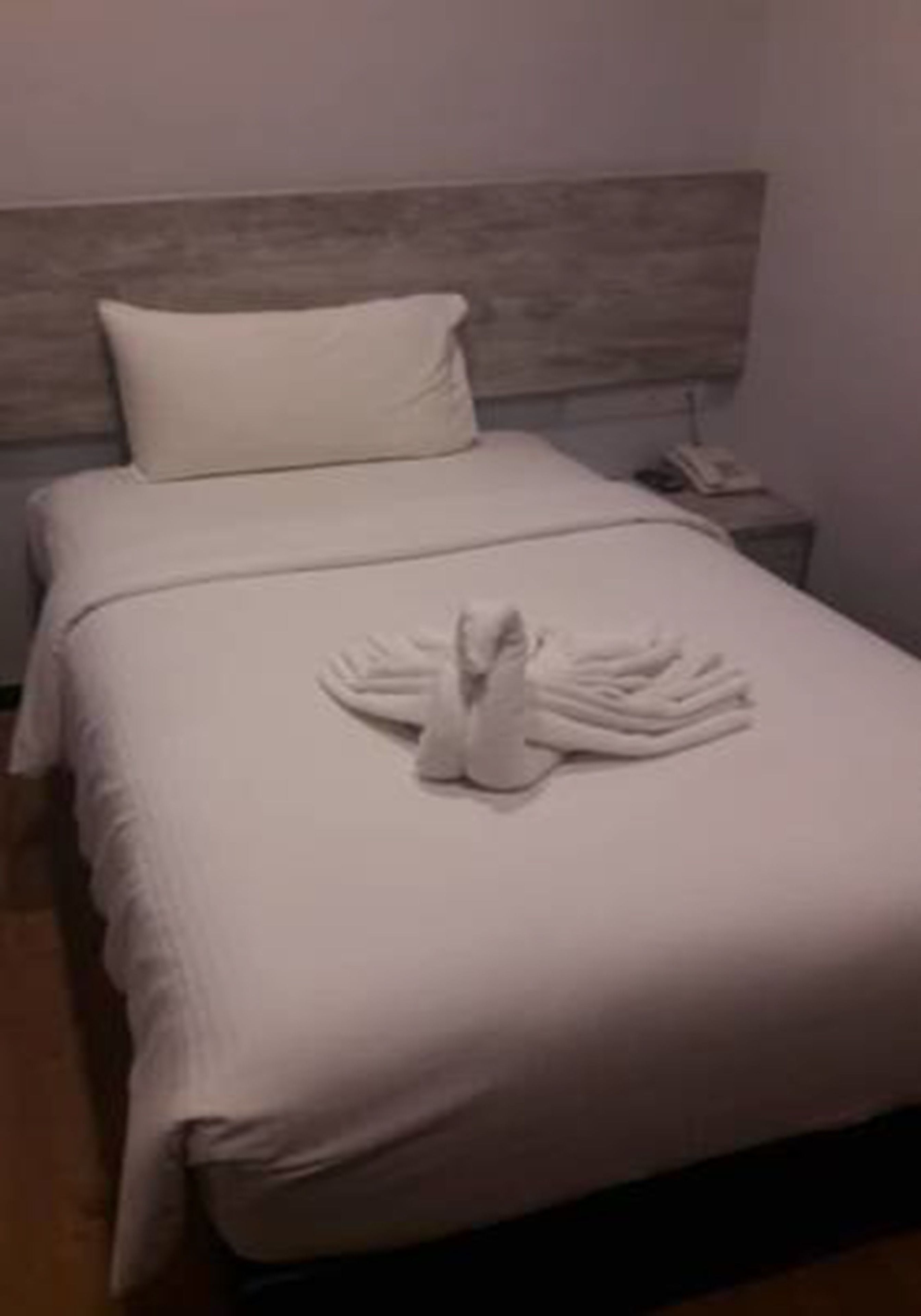 A neatly made bed with a towel arranged in a swan shape, a pillow, and a wooden headboard.