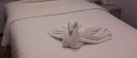 A neatly made bed with a towel arranged in a swan shape, a pillow, and a wooden headboard.