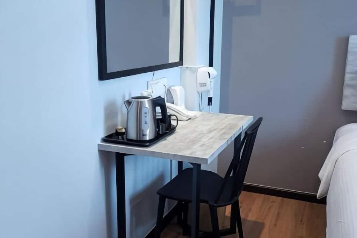 Een kleine hotelkamer met kitchenette, een bed, een stoel en een spiegel.
