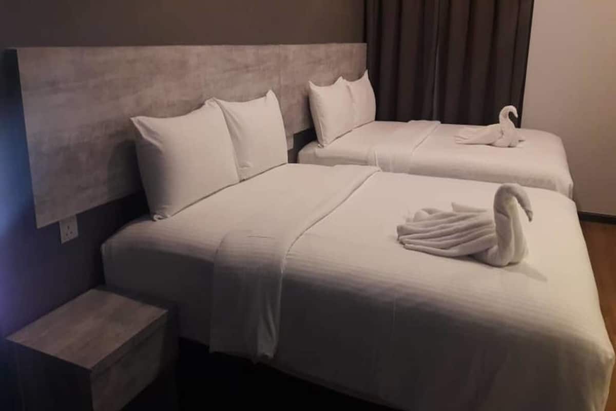 Een hotelkamer met twee bedden, elk met witte beddengoed en kussens. Er liggen twee zwaan-vormige handdoeken op de bedden.