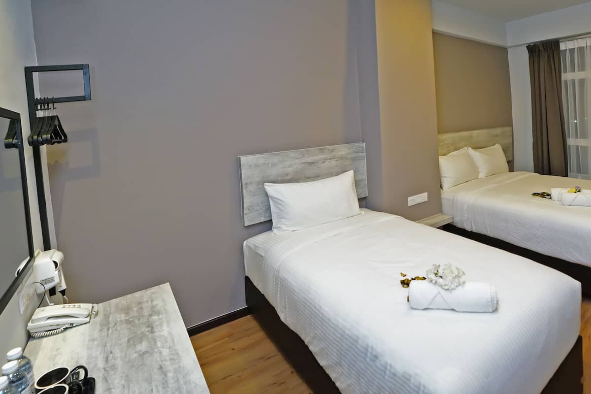 Een hotelkamer met twee bedden, een bureau met telefoon en toiletartikelen, en een aan de muur bevestigde televisie.