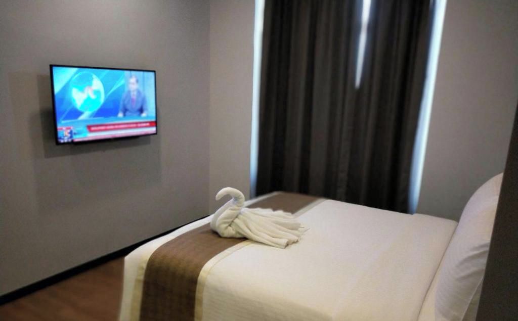 A hotel room with a bed, a TV mounted on the wall, and a window with curtains.