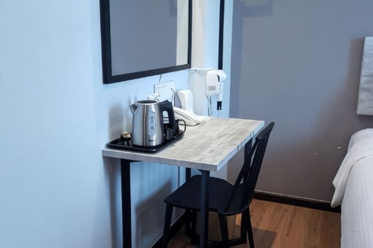 Una habitación de hotel pequeña con kitchenette, cama, silla y espejo.