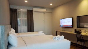 Quarto de hotel com uma cama grande, uma escrivaninha com computador e televisão na parede.