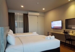 Una habitación de hotel con una cama grande, un escritorio con computadora y un televisor en la pared.