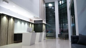 Uma área de recepção moderna com um balcão branco, um sofá e uma grande janela com vista para o exterior.