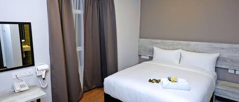 A hotel room with a bed, a bedside table with a phone, a mirror, and a window with curtains.