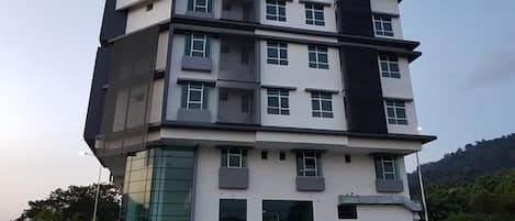 A multi-story building with a modern architectural design, featuring a combination of white and dark grey colors, large windows, and a flat roof.