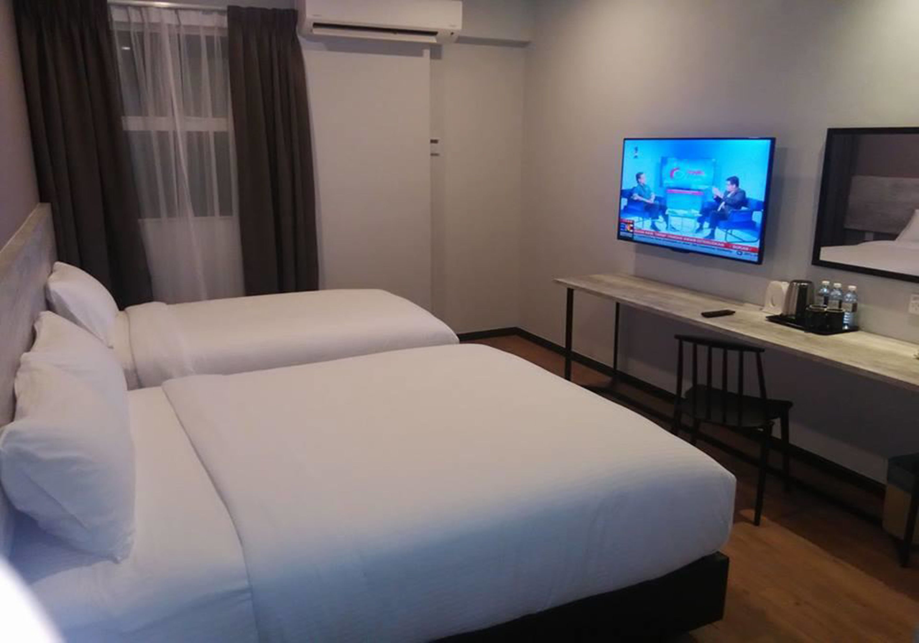 Habitación de hotel con dos camas, un televisor en la pared, un escritorio con una silla y una ventana con cortinas.