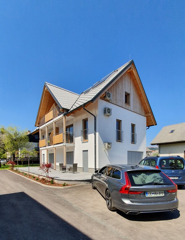 Uma casa moderna de dois andares com telhado inclinado, uma varanda no andar de cima e um carro estacionado na entrada.