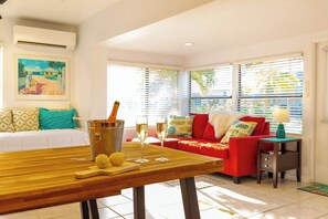 A room with a wooden table, a red sofa, and a bed with patterned pillows.