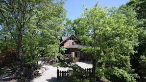 A cabin surrounded by dense trees, with a gravel driveway leading to the entrance. - Suitaikyou (Nasu)